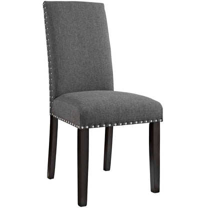 Grey fabric dining side chair with tall back, dark wood legs, and silver nailhead trim along seat and back edges.