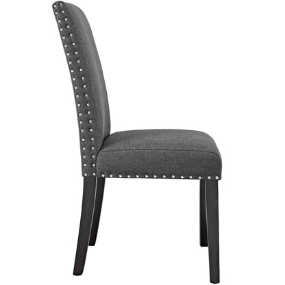 Gray fabric dining chair with nailhead trim along edges, padded back and seat, dark wooden tapered legs.
