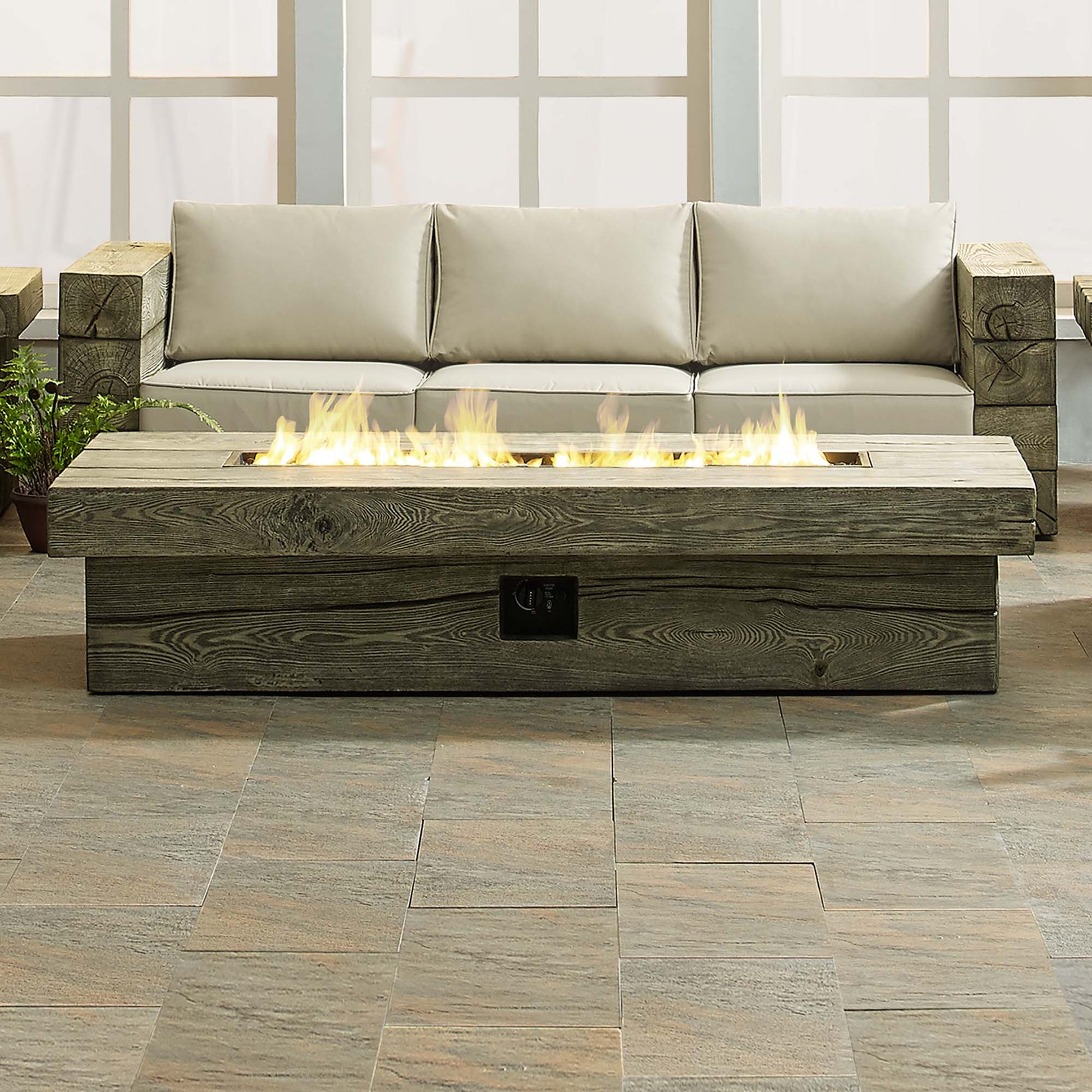 Rectangular gray wood-look fire pit table with flames on a tiled outdoor patio.