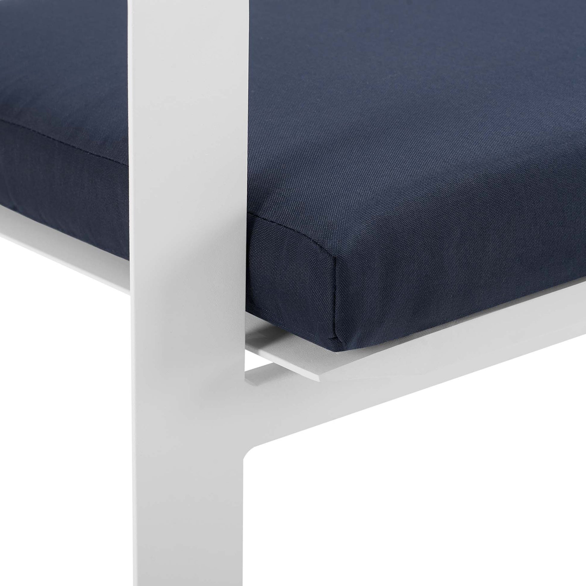White aluminum-framed outdoor dining armchair with navy cushion; close-up of seat edge and leg.