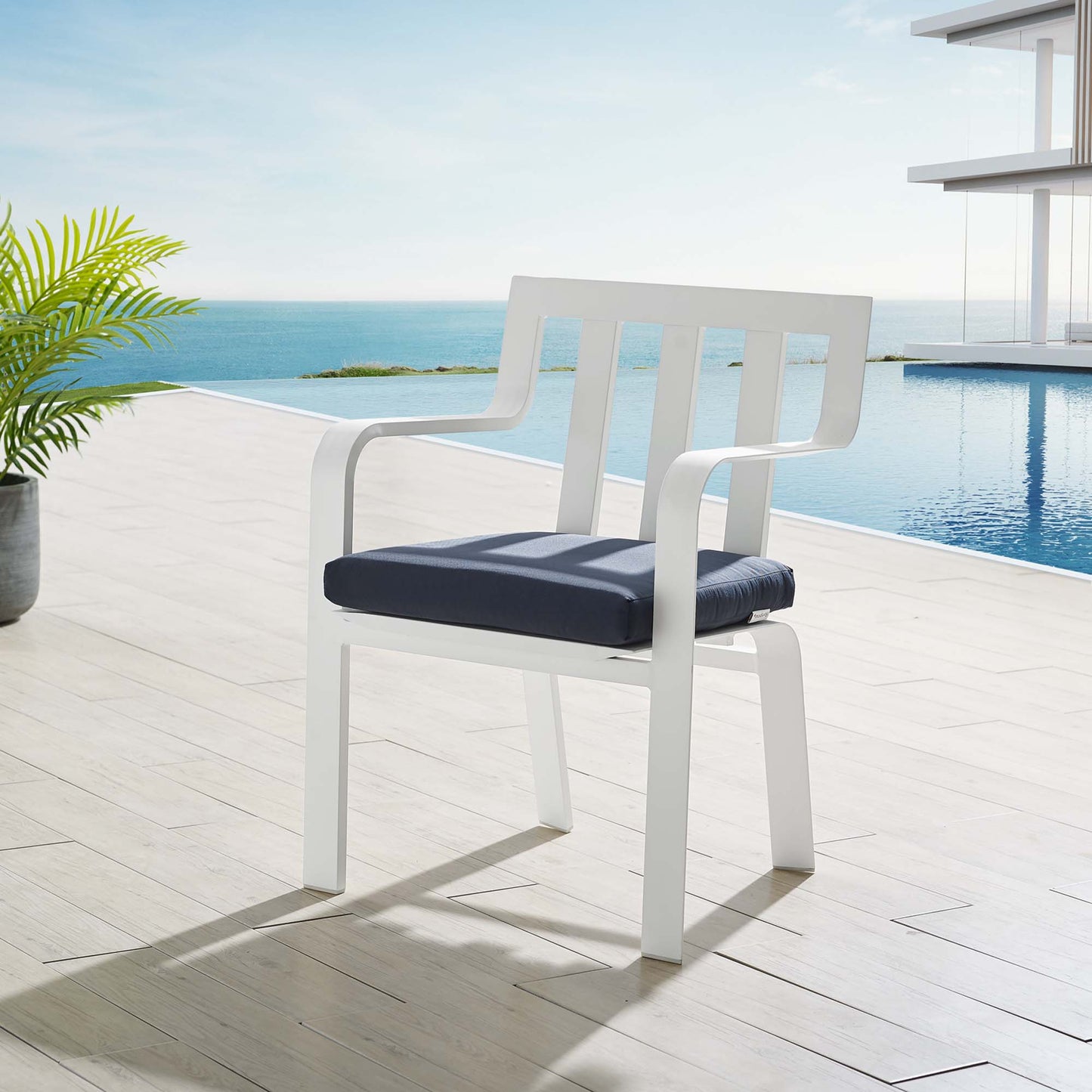 White outdoor chair with navy cushion on a wooden pool deck overlooking the ocean.