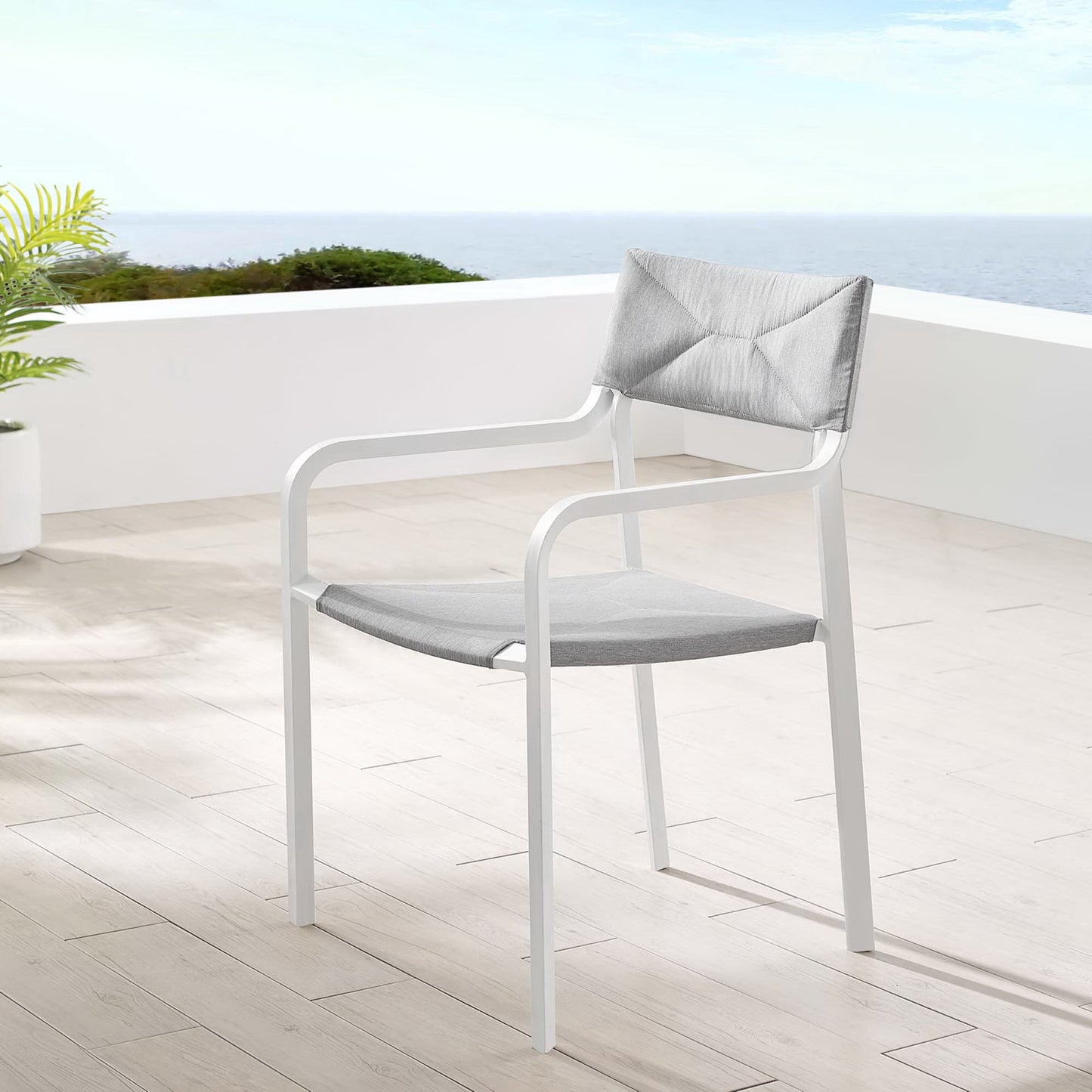 White outdoor armchair with gray seat cushion and gray back pillow on a terrace with ocean view.