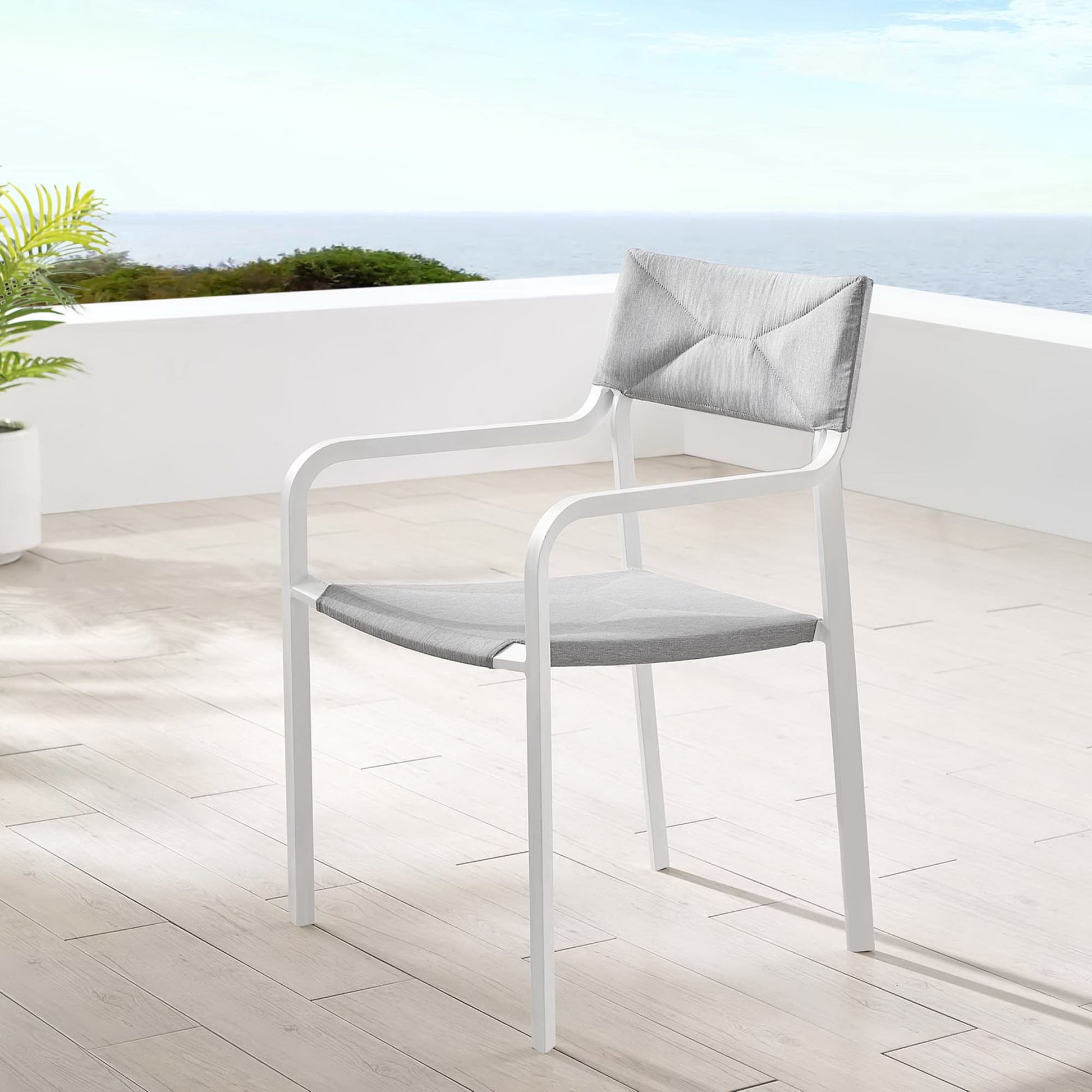 White outdoor armchair with gray seat cushion and gray back pillow on a terrace with ocean view.