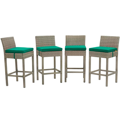 Set of four bar stools with beige wicker frames and teal cushions and footrests for outdoor seating.