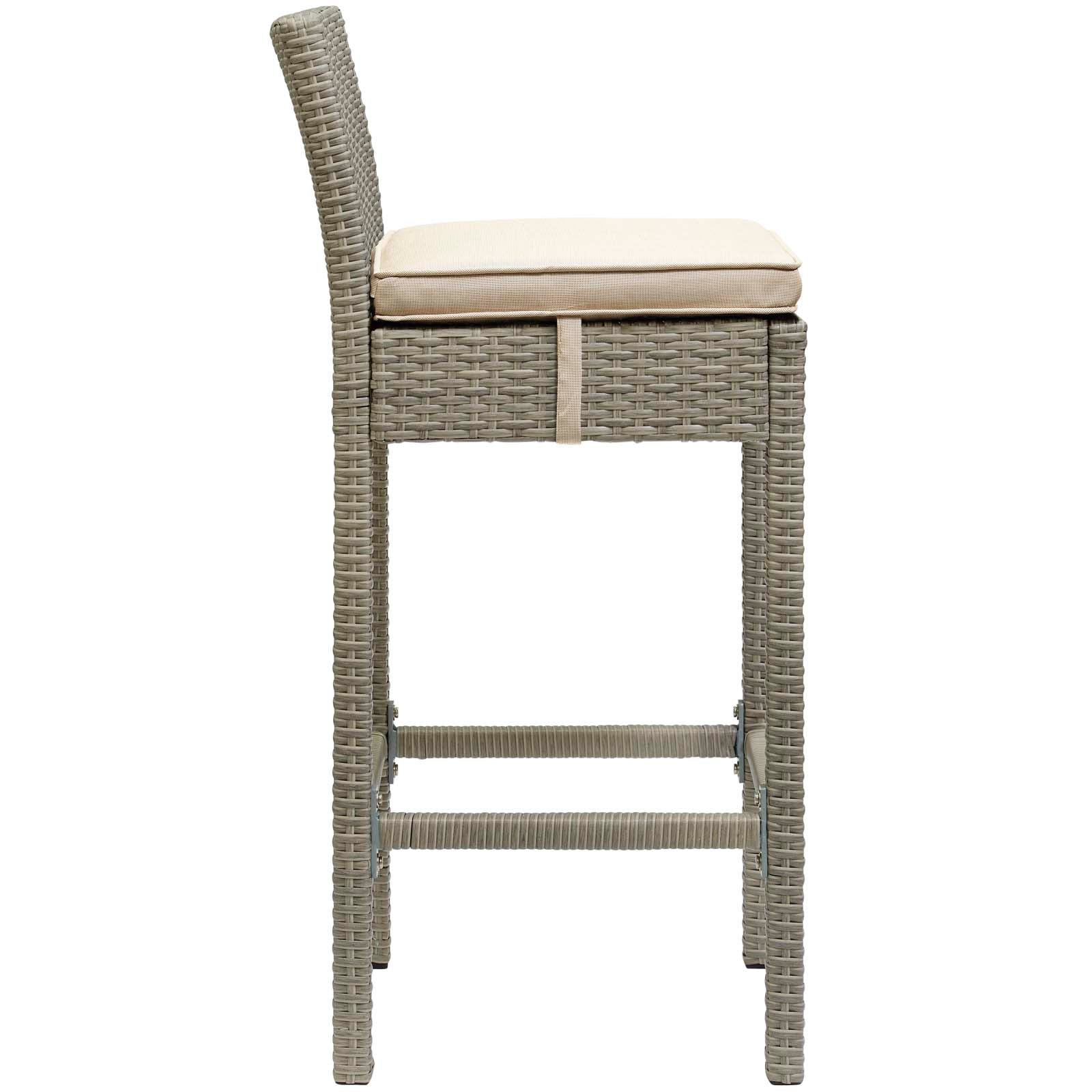 Gray-brown woven rattan bar stool with tall back, beige seat cushion and woven footrest bars.