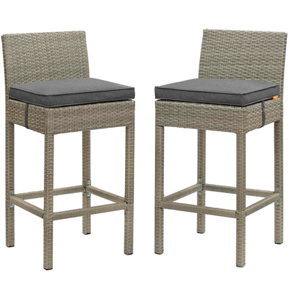 Pair of light gray wicker bar stools with charcoal cushions, high backs, and metal foot rails for outdoor use.