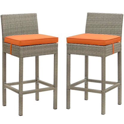 Two gray wicker bar stools with orange cushions, square seats, high backs, metal foot rails for outdoor patio use.