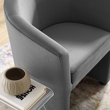 Light gray upholstered armchair with curved arms, paired with a ribbed beige ceramic vase on a white side table.