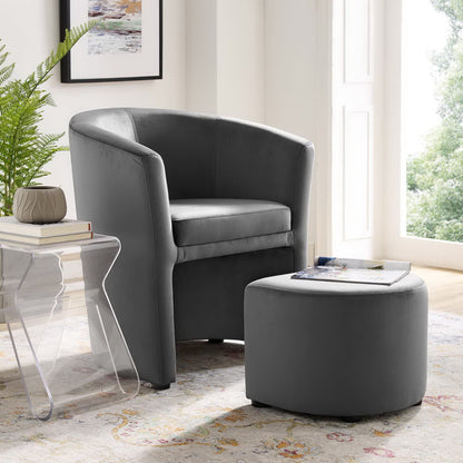 Gray upholstered arm chair and matching ottoman in a modern living room, beside a glass side table.
