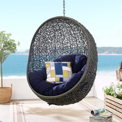 Dark gray fabric swing outdoor patio lounge chair without stand with navy cushions and a geometric blue-yellow pillow on a seaside patio.