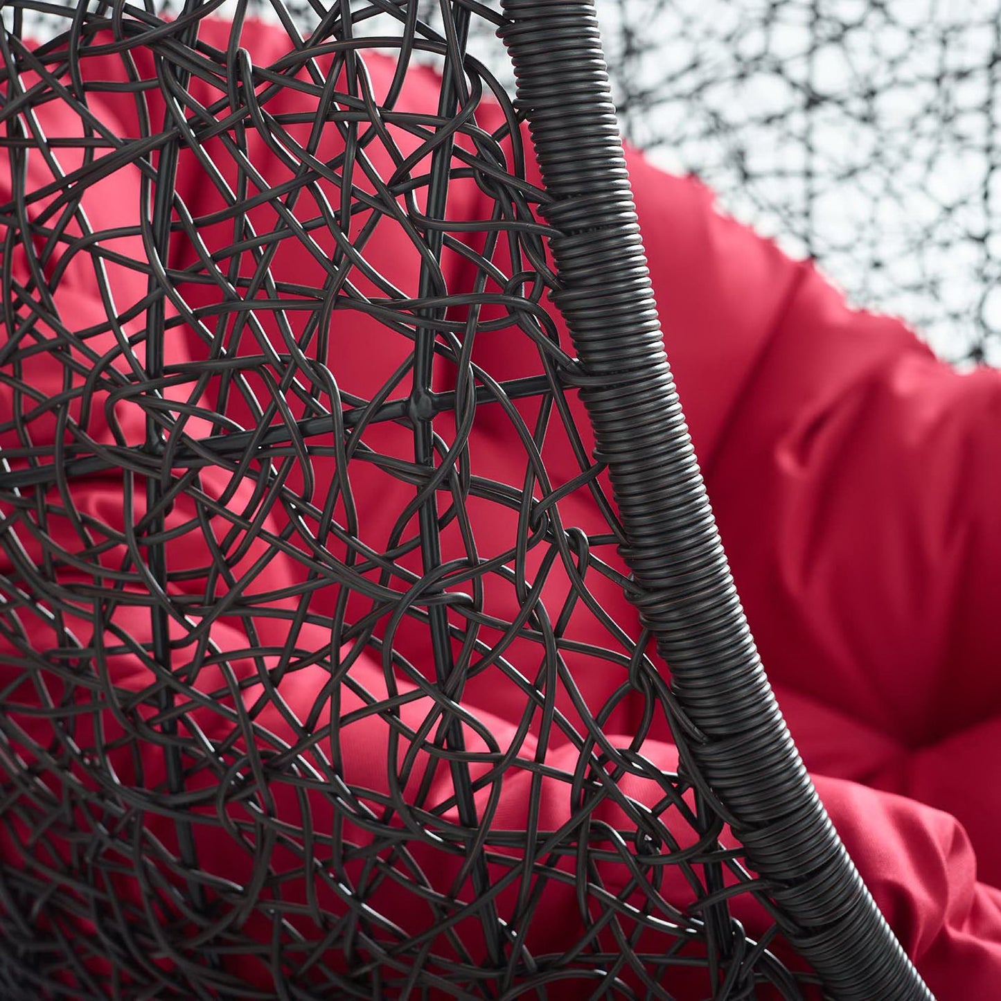 Close-up of a black metal woven chair back with tangled lattice, red cushion visible in the background.