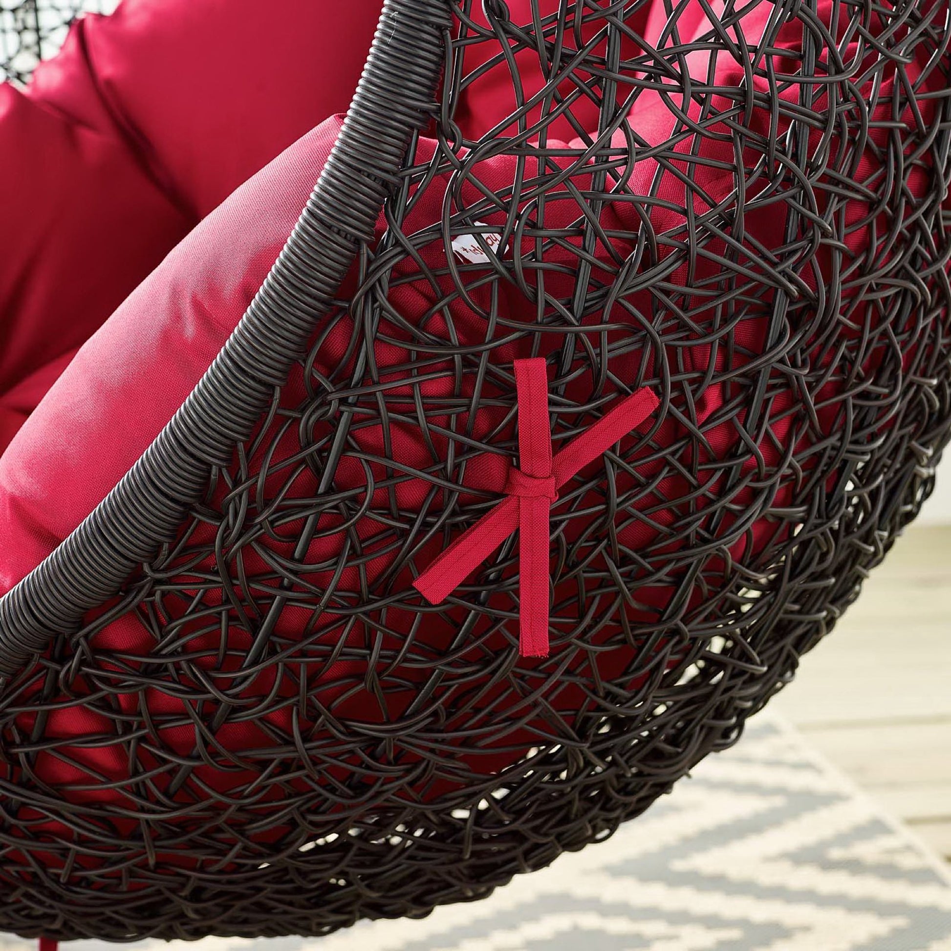 Black woven rattan hanging chair with red cushions and a red ribbon accent.