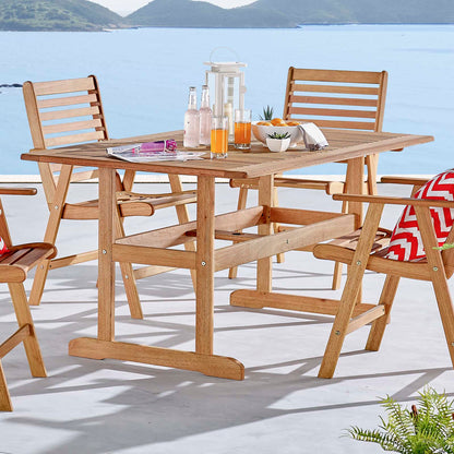 Natural wood outdoor rectangular dining table on a lakeside patio with bottles and bowls.