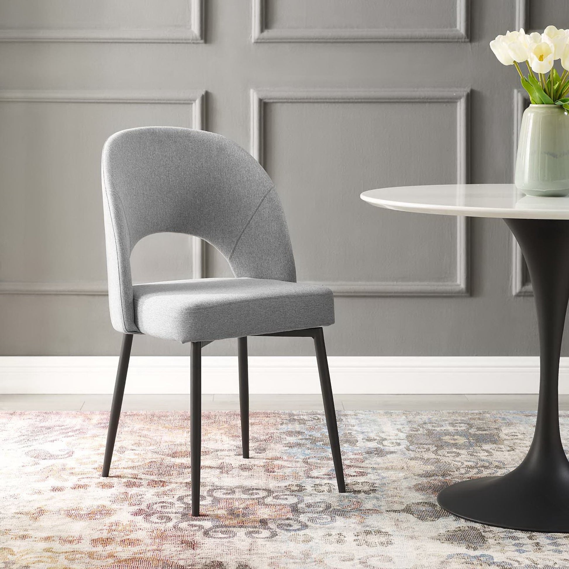Light gray upholstered dining chair with curved back and black legs beside a round white table with a black pedestal.