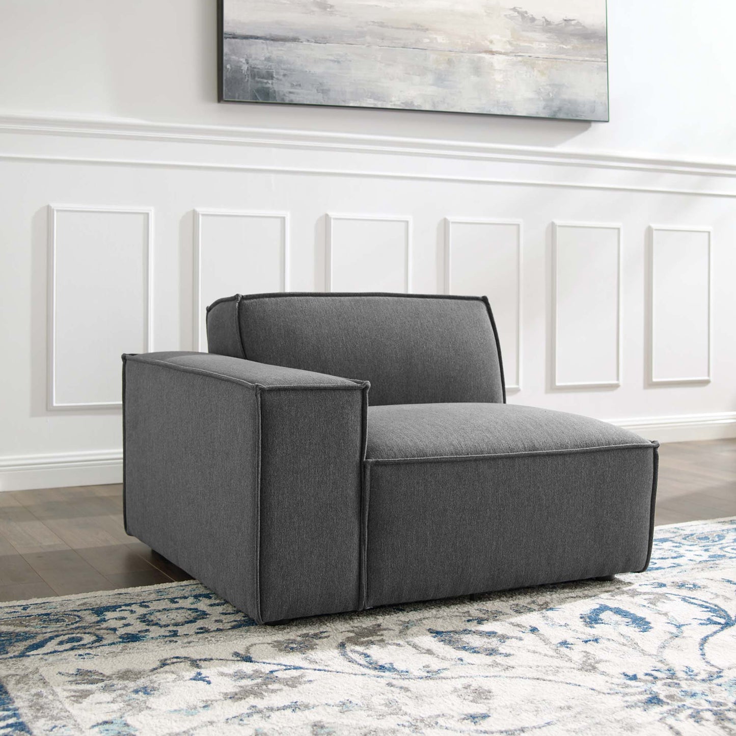 Charcoal gray, boxy modular armchair with wide arms; modern fabric upholstery in a living room with a blue patterned rug.