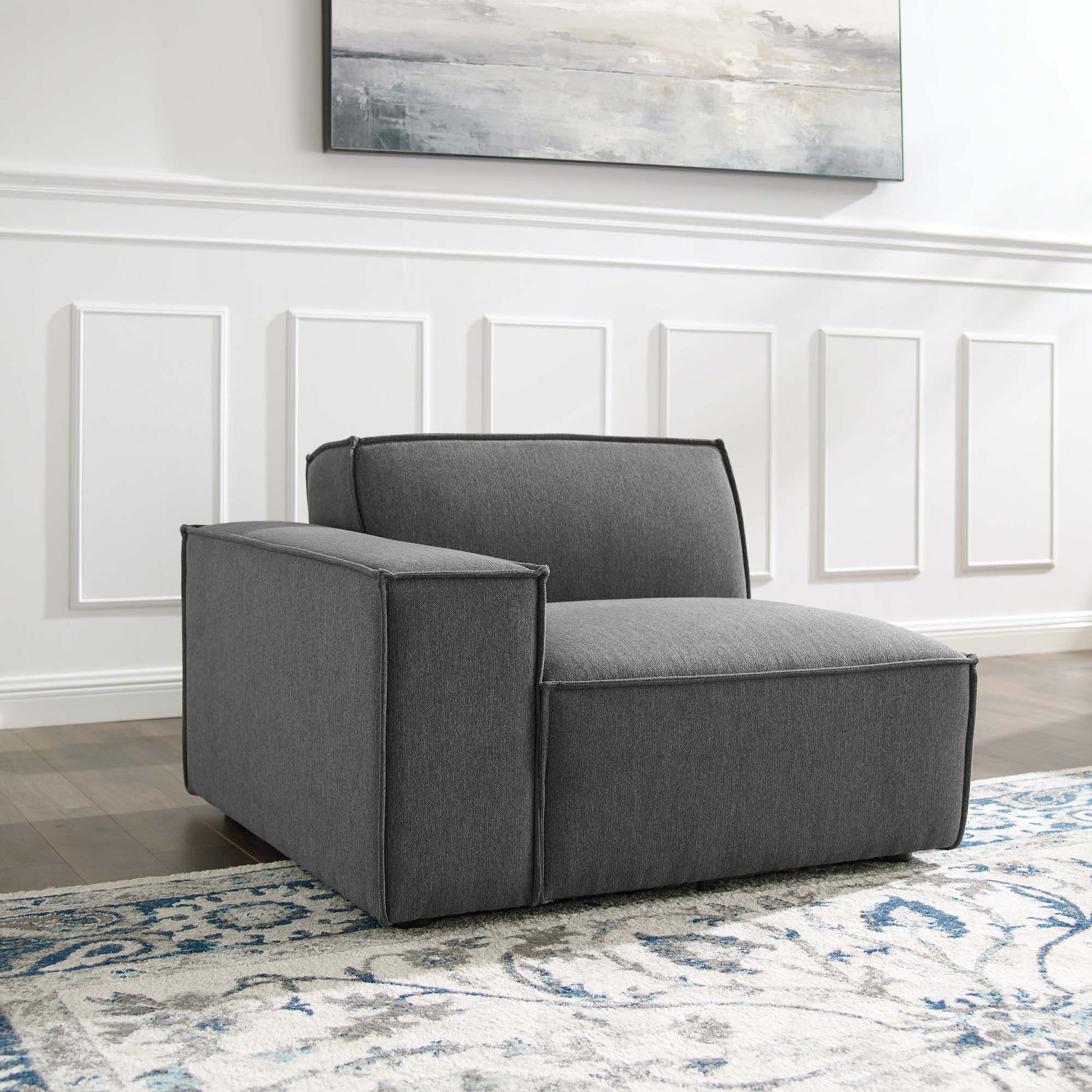 Charcoal gray, boxy modular armchair with wide arms; modern fabric upholstery in a living room with a blue patterned rug.