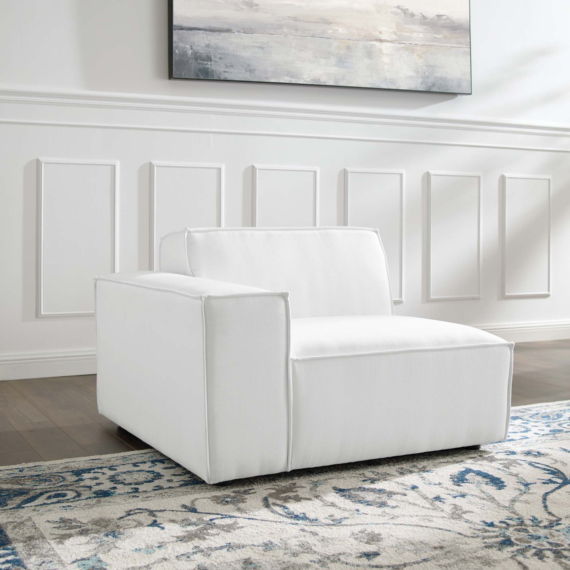 White upholstered modern armchair with boxy arms and low back, on a blue and white patterned rug in a bright paneled room.