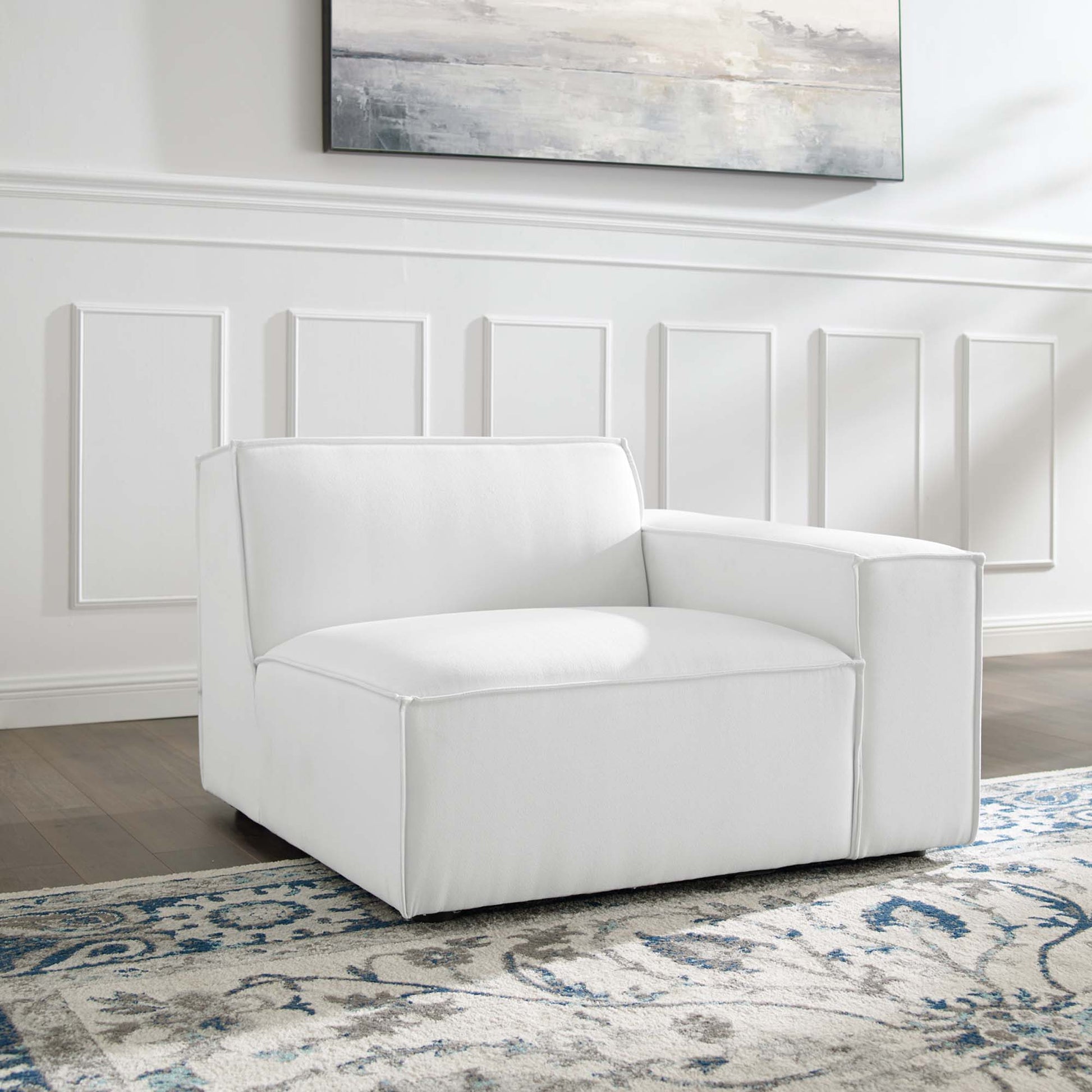 White modern upholstered armchair with square cushions in a white-paneled living room on a blue patterned rug.