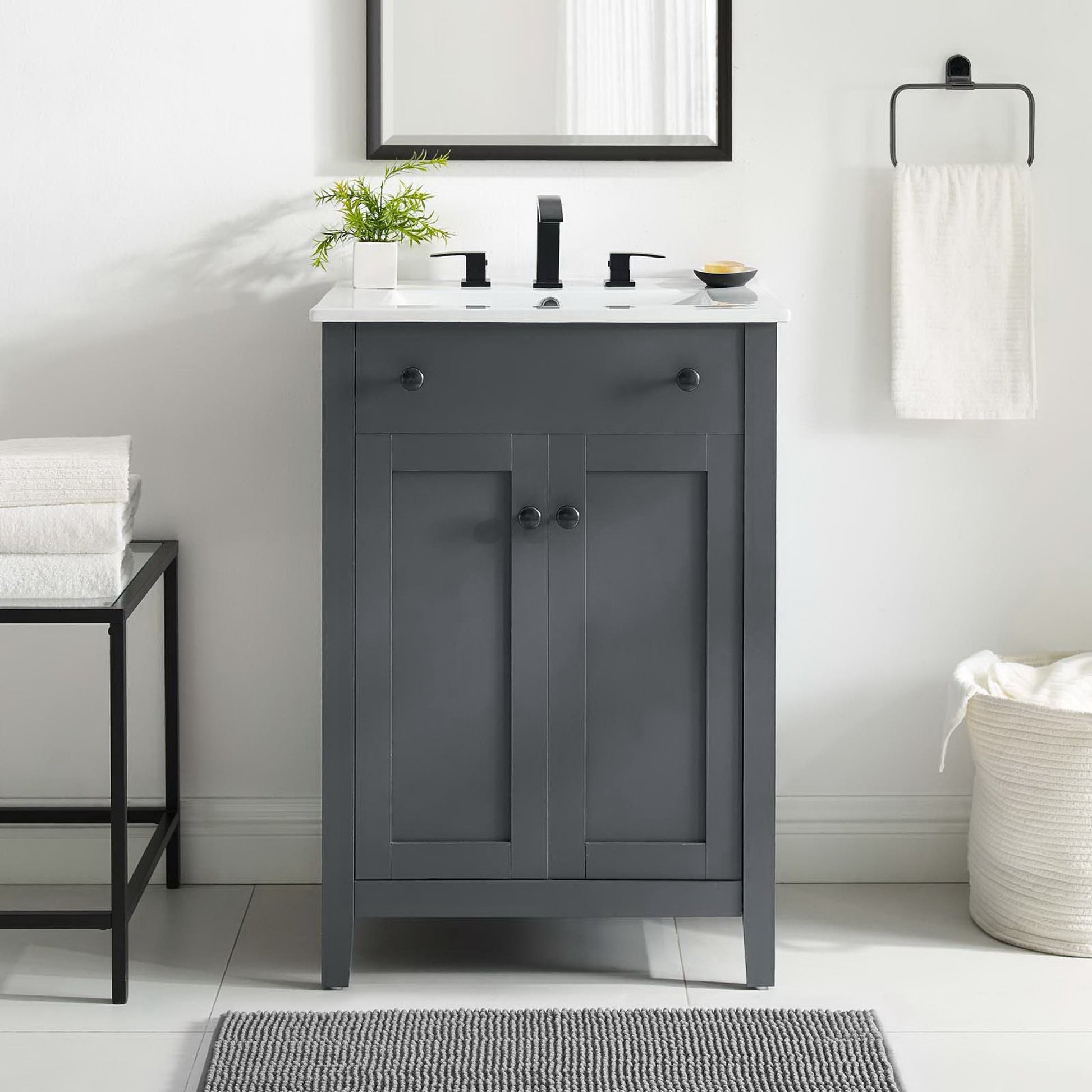 Gray shaker-style bathroom vanity with white countertop, black faucet, two-panel doors and knobs, plant and mirror above.