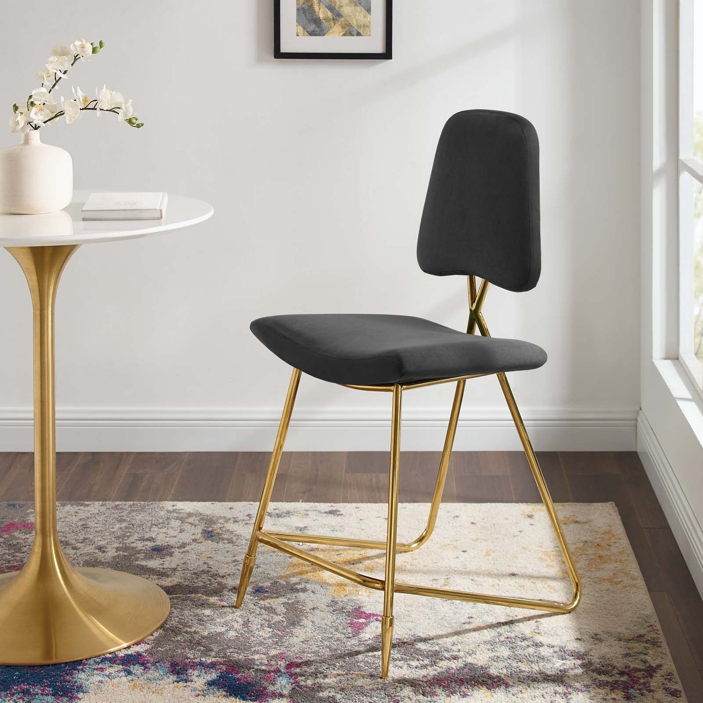 Black velvet counter stool with gold sled legs in a modern bright room beside a white round table.