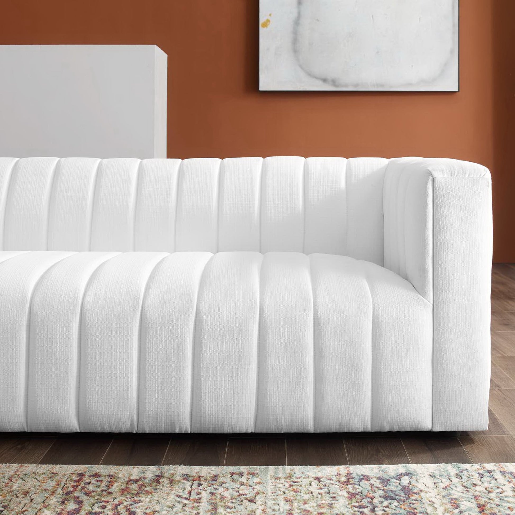 White modern sofa with vertical channel tufting and low-profile arms on a wooden floor.