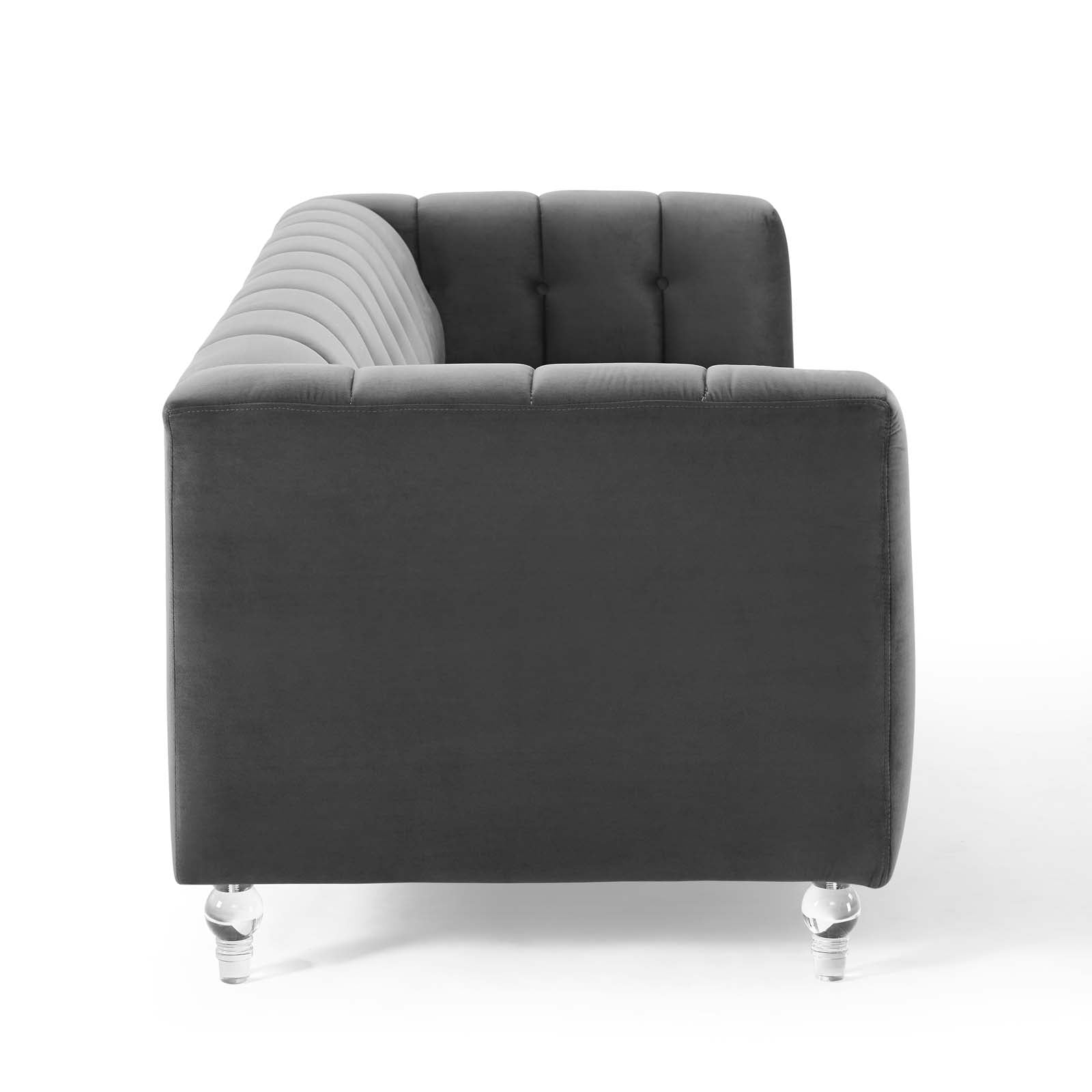 Charcoal gray velvet tufted corner sofa with a light gray curved backrest on the left and clear acrylic legs.