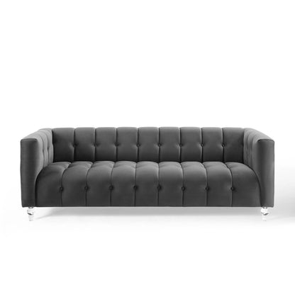 Dark gray tufted sofa with button upholstery, low arms, Chesterfield-inspired silhouette, clear acrylic legs.