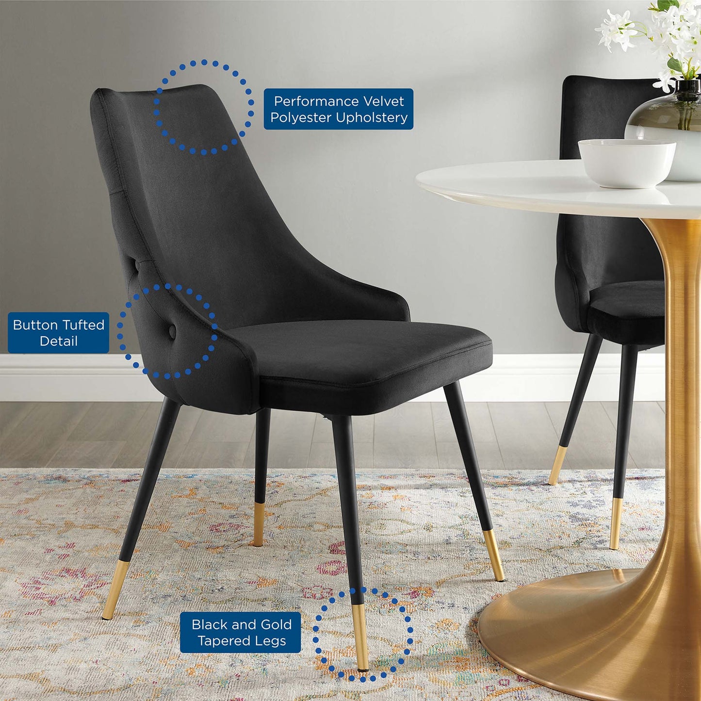 Black velvet dining chairs with button tufting and gold-tipped tapered legs, shown around a round white pedestal table.