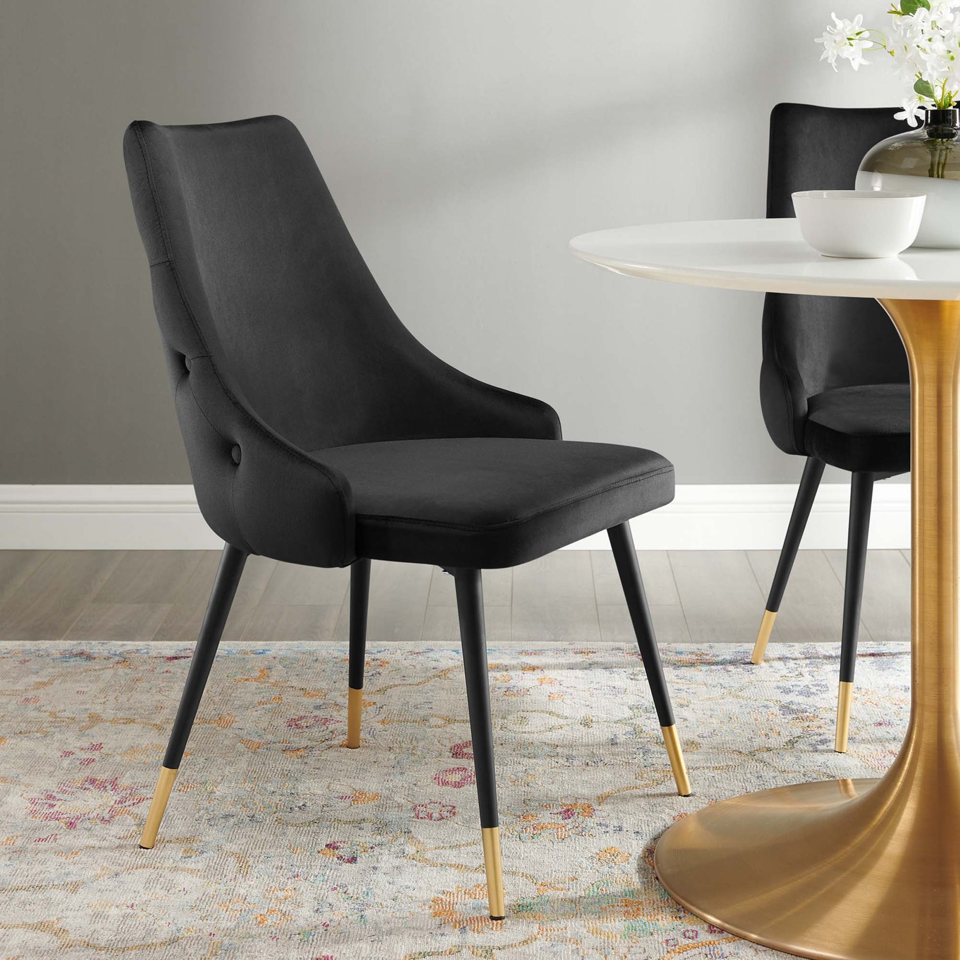 Two black upholstered dining chairs with curved backs and gold-tipped legs around a white round table with a gold pedestal.