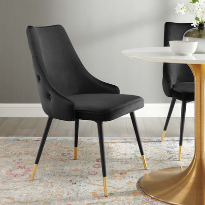 Two black upholstered dining chairs with curved backs and gold-tipped legs around a white round table with a gold pedestal.