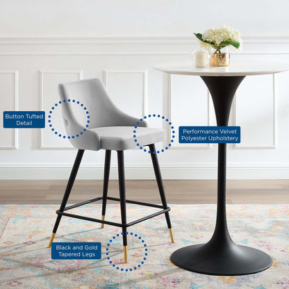 Light gray button-tufted velvet counter stool with black tapered legs and gold tips beside a white round pedestal table.