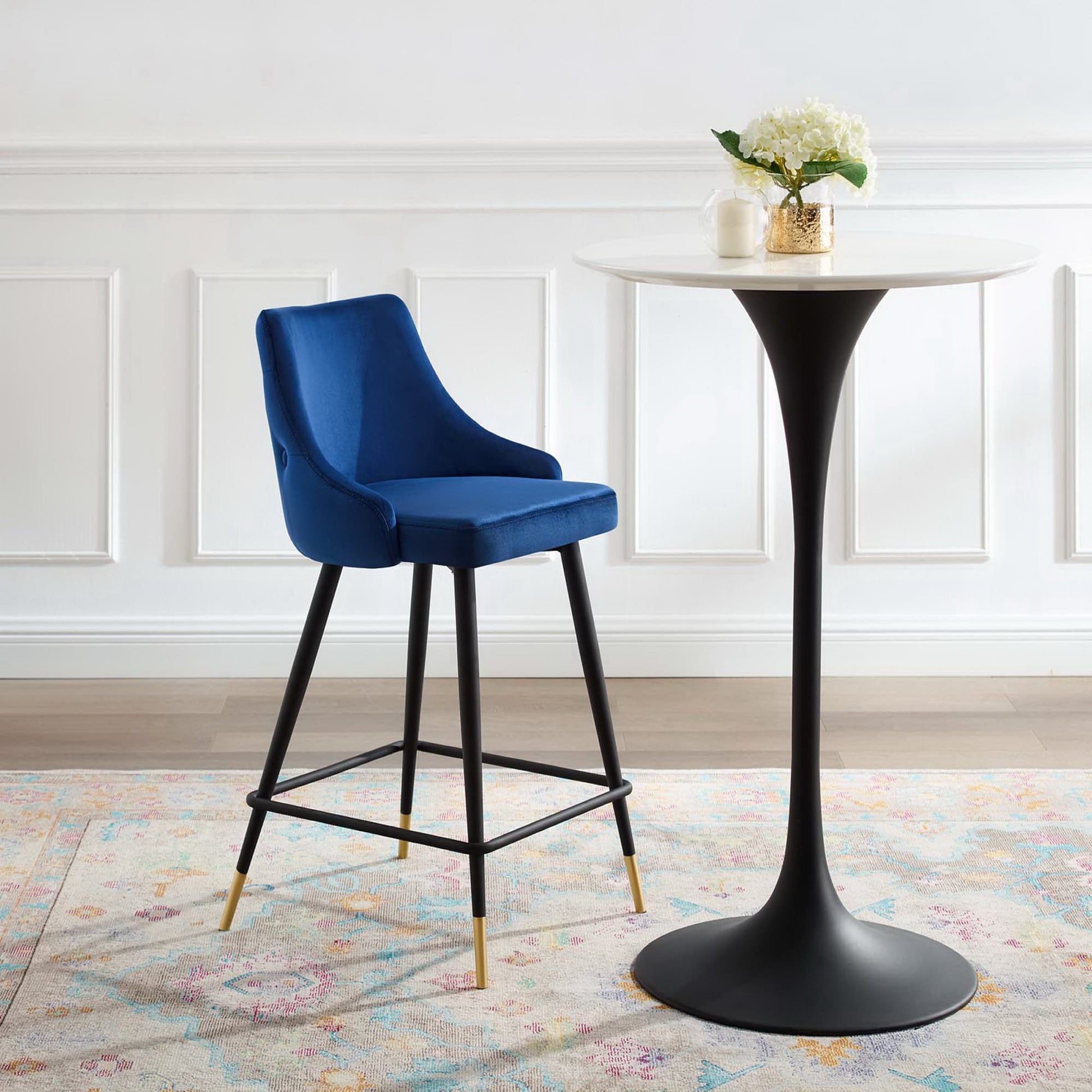 Navy velvet counter stool with black metal legs and brass caps beside a round white marble-top table.