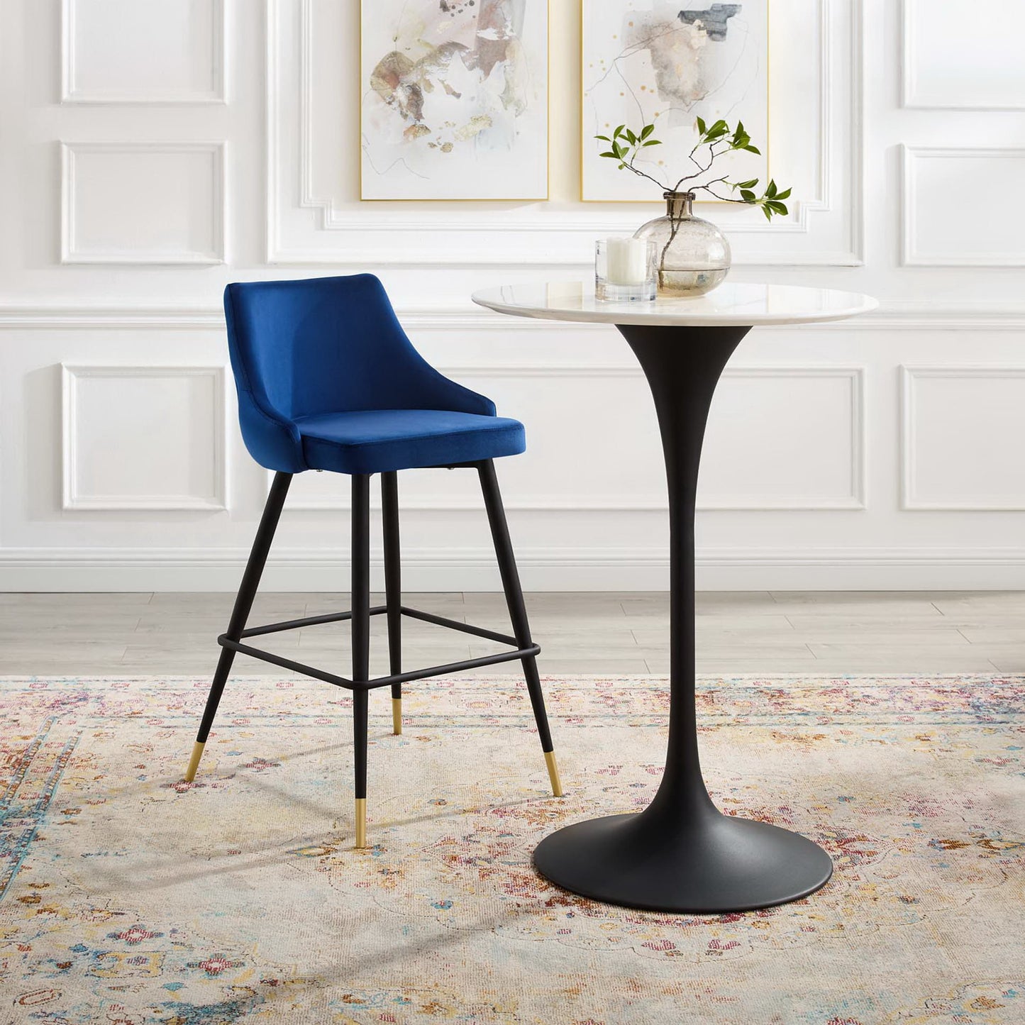 Navy blue velvet bar stool with black legs and gold caps beside a round white marble-top table in a white paneled room.