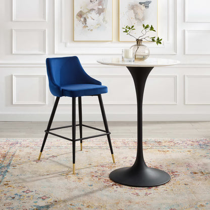 Navy blue velvet bar stool with black legs and gold caps beside a round white marble-top table in a white paneled room.