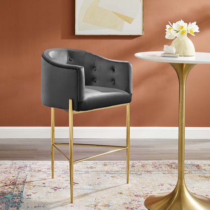 Charcoal tufted velvet bar stool with gold metal legs beside a white round pedestal table