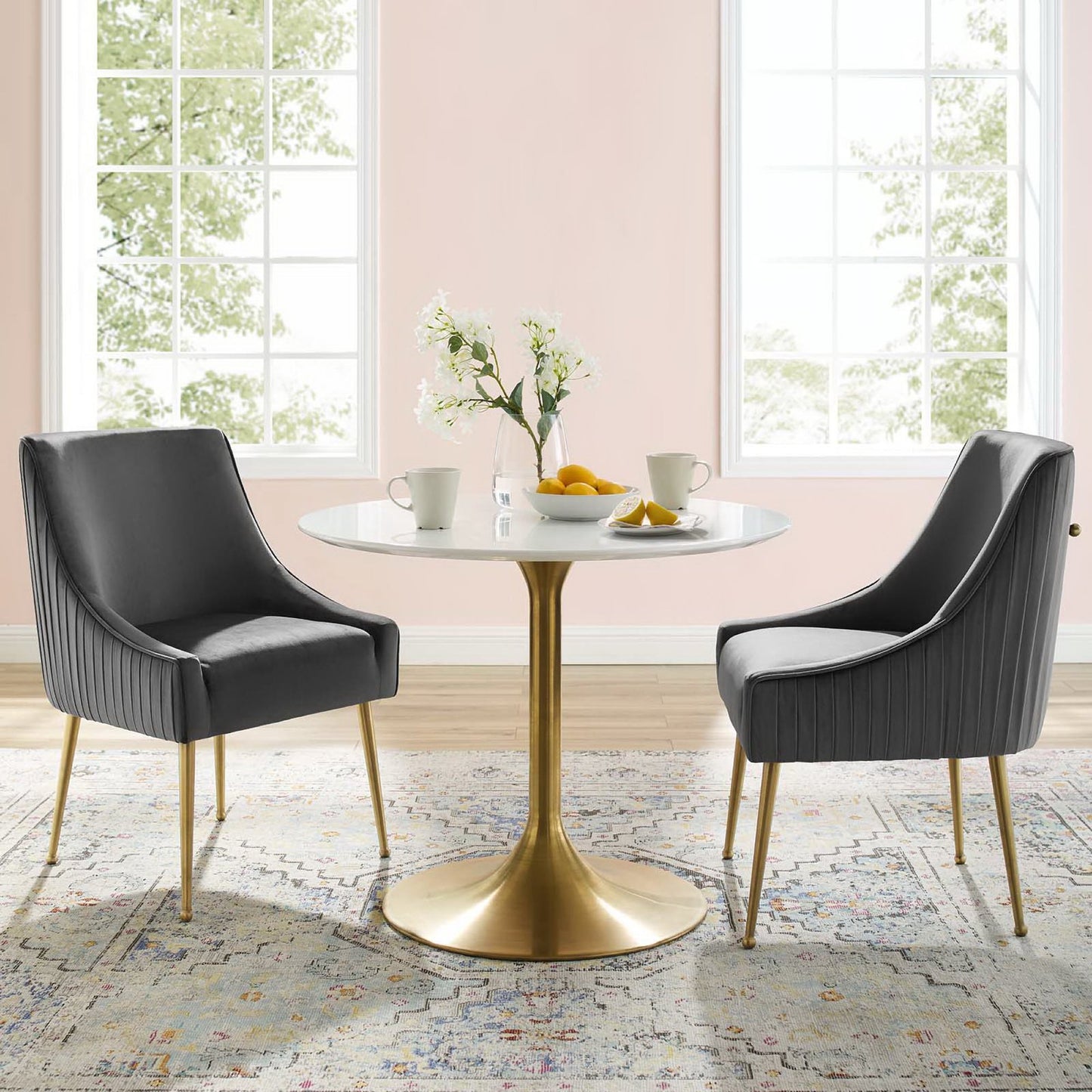 Two gray upholstered dining chairs with gold legs in a sunlit pastel room.