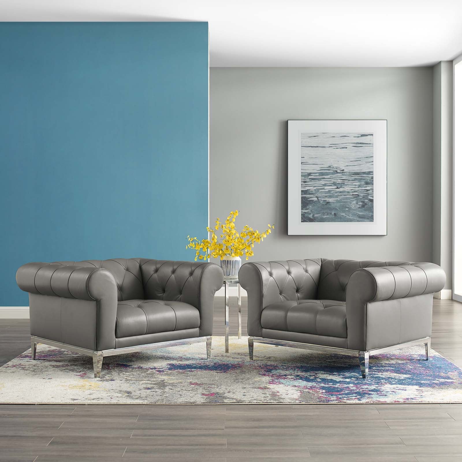 Gray tufted leather armchairs with metal legs in a modern living room, blue wall, yellow flowers, framed seascape, rug.