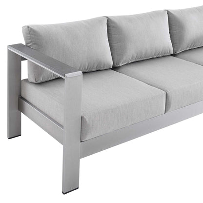Gray framed sofa with thick light-gray cushions; modern boxy arms, outdoor lounge seating.