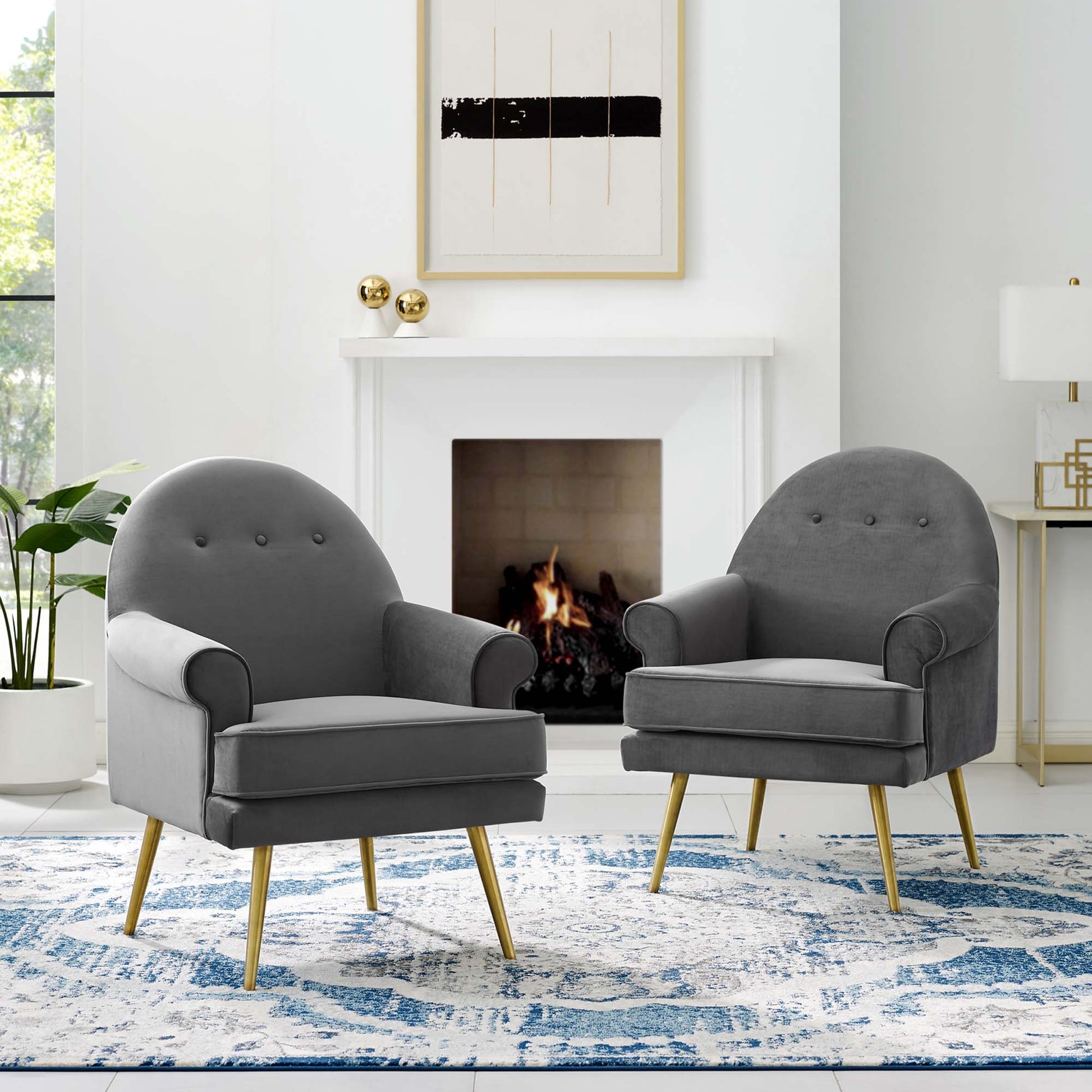 Pair of grey tufted armchairs with light wooden legs in a bright living room beside a white fireplace and blue patterned rug.