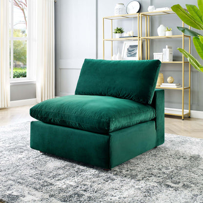 Emerald green velvet armless chair with thick cushions in a modern living room with gold shelving and a large plant.