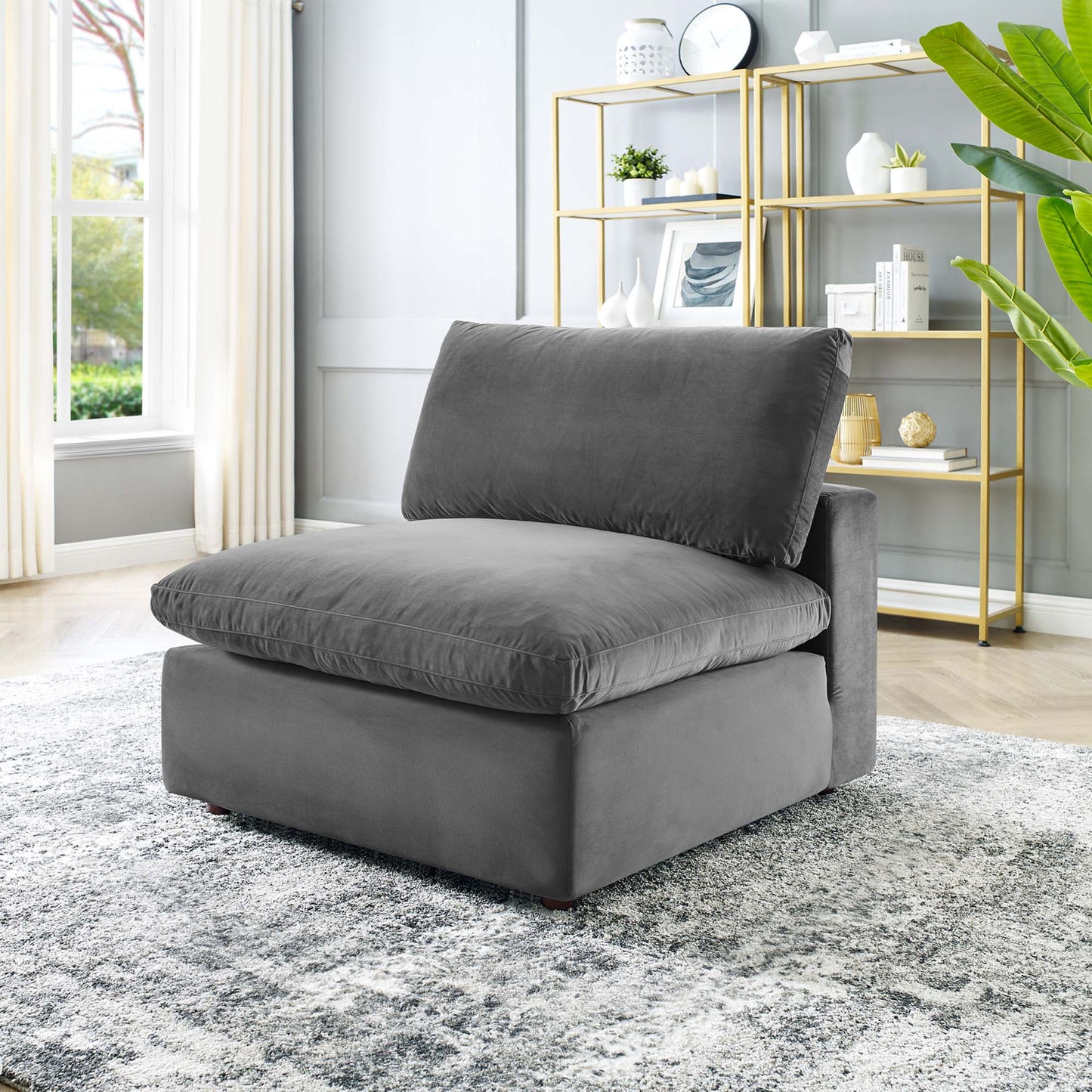 Grey velvet armless lounge chair with thick seat and back cushions, low-profile modern design in a bright living room.