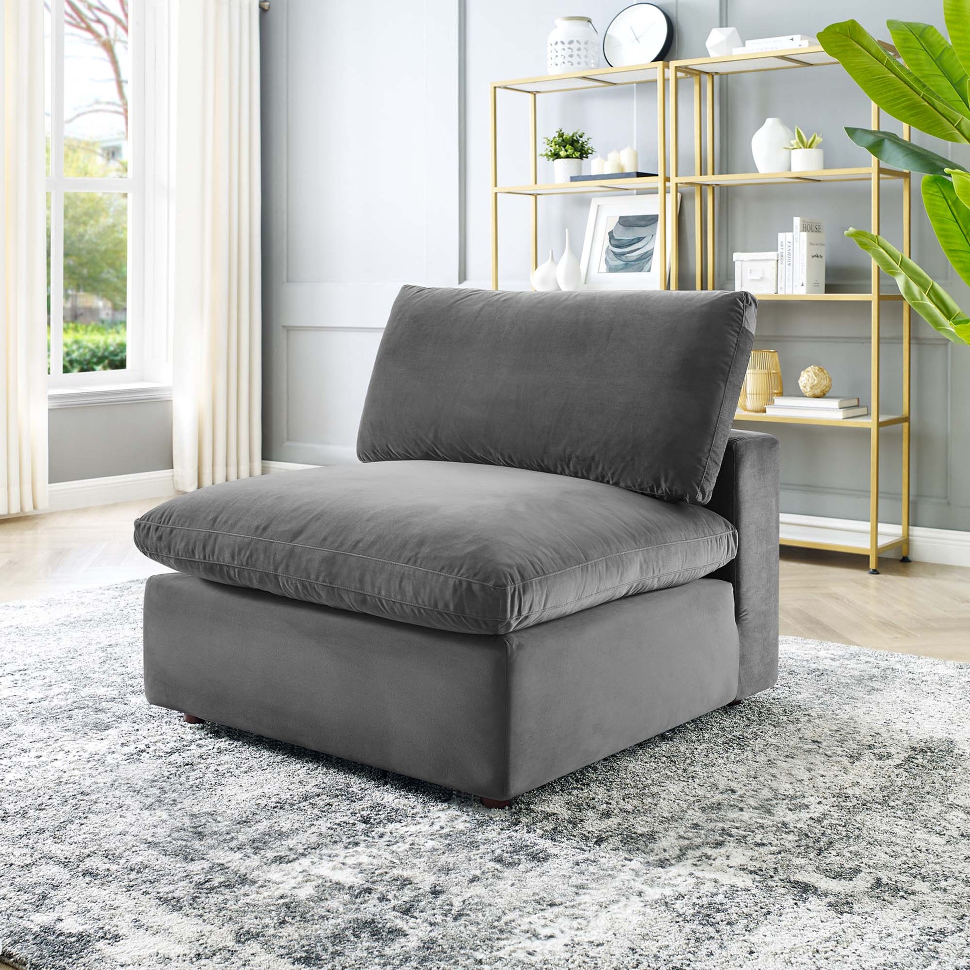 Grey velvet armless lounge chair with thick seat and back cushions, low-profile modern design in a bright living room.
