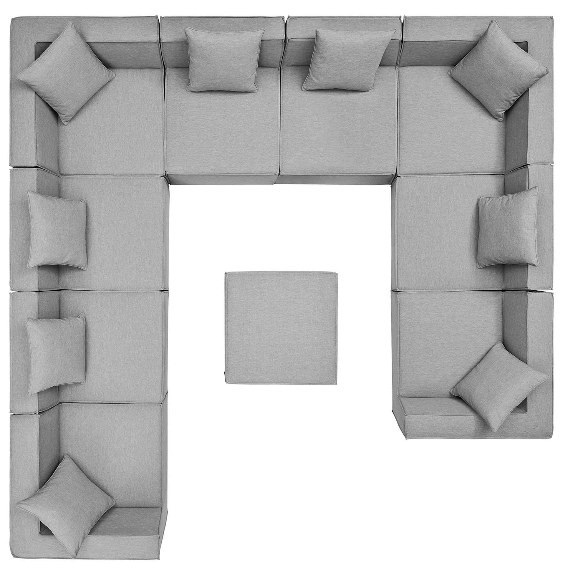 Gray modular sectional sofa in a U-shaped arrangement with plush cushions and a central ottoman, fabric upholstery.