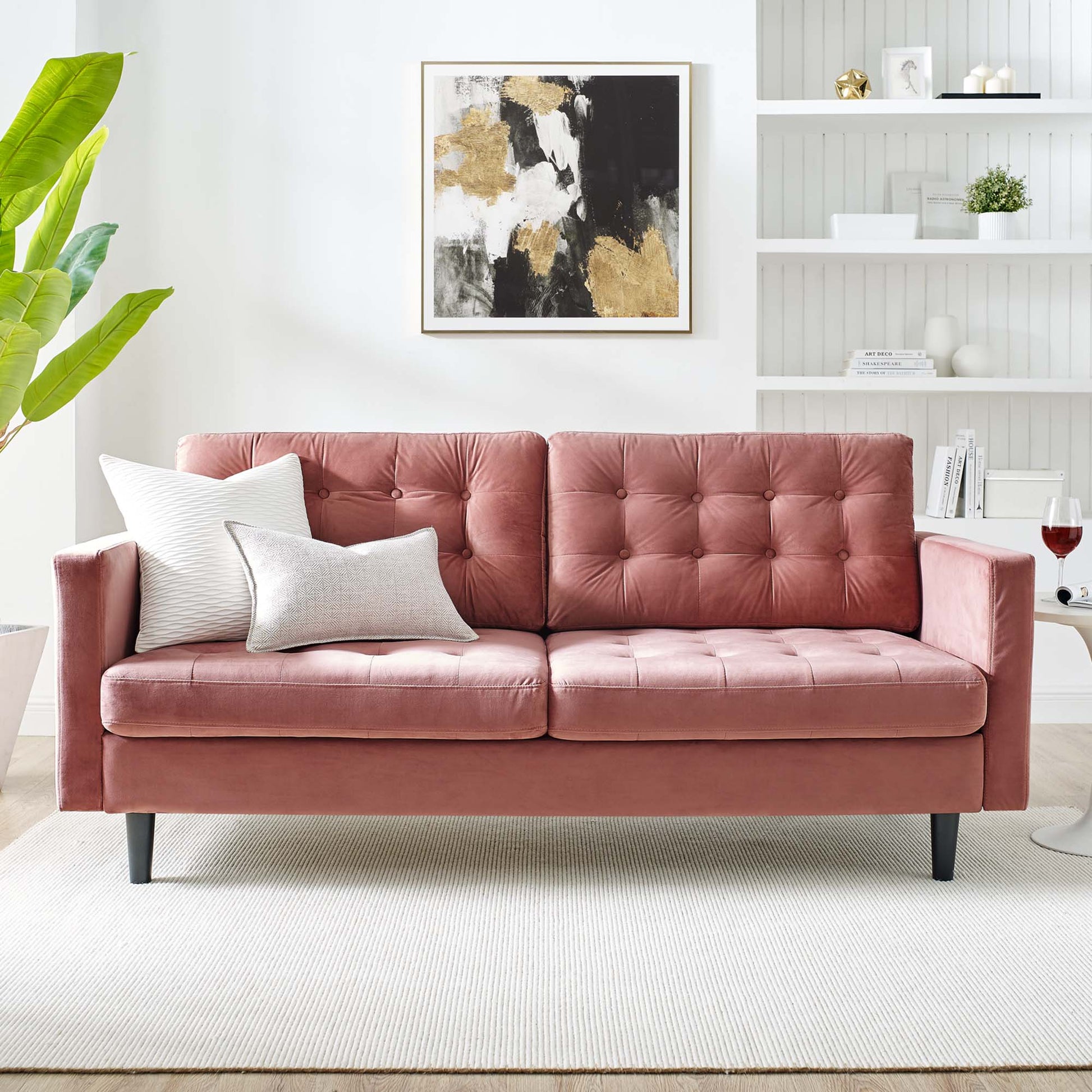 Dusty-rose velvet tufted 3-seat sofa with square arms and dark tapered legs, white/gray pillows in a bright living room.