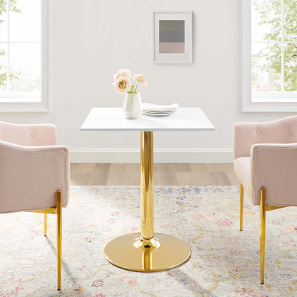 White square table with gold pedestal base, blush pink chairs with gold legs, vase of flowers, pastel rug.