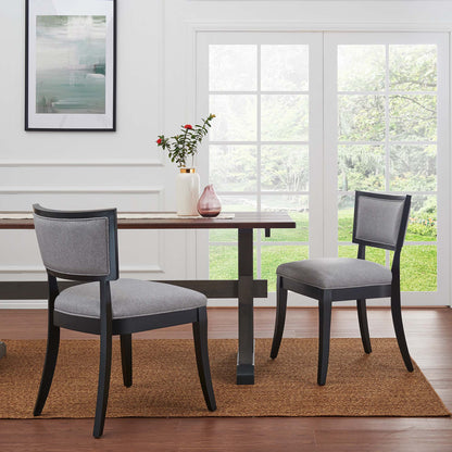 Two grey upholstered dining chairs on a jute rug by glass French doors, with a vase centerpiece.