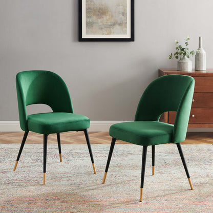 Two emerald green velvet dining side chairs with curved backs and black metal legs with gold tips, chic mid-century style.