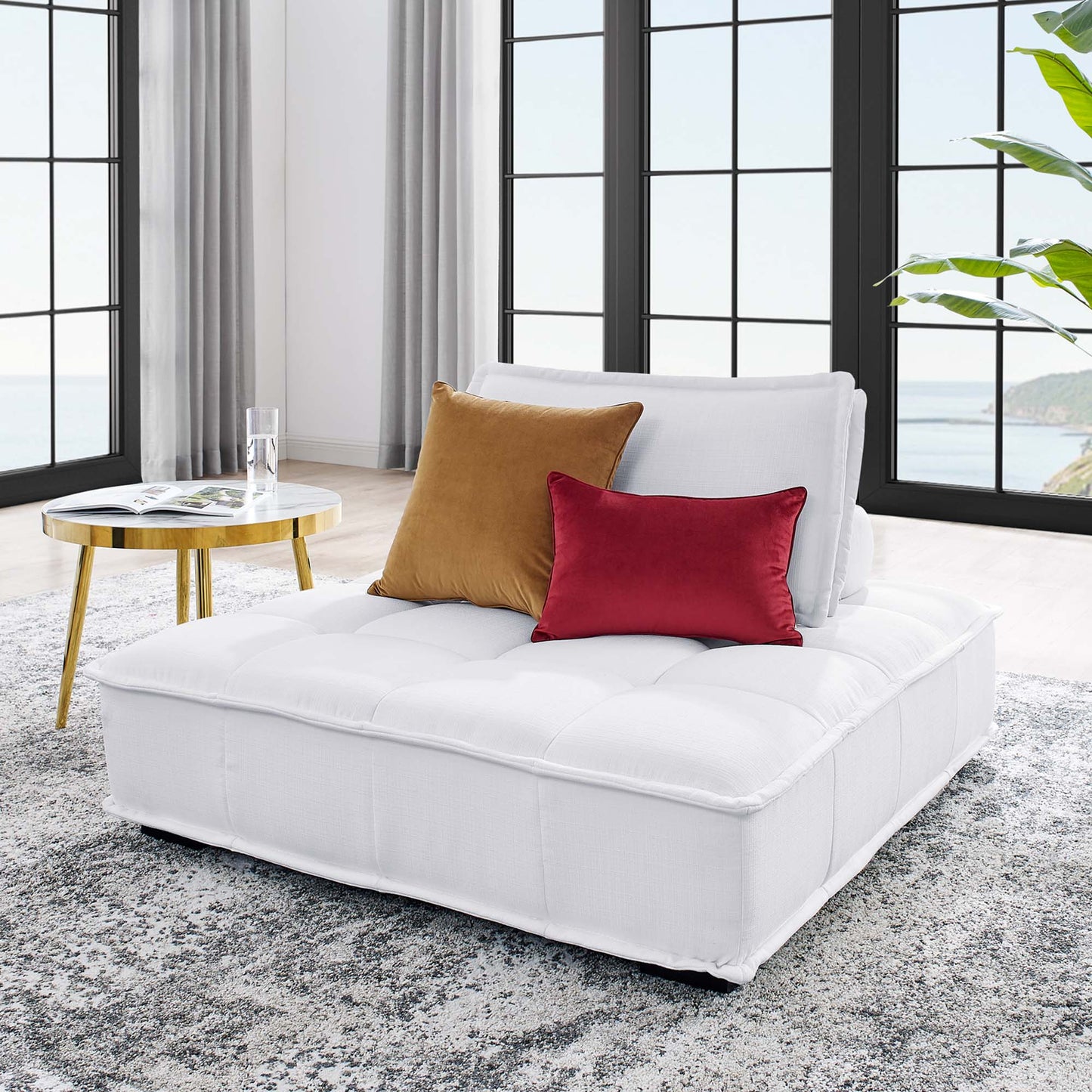 White tufted armless chair in a bright modern living room with black-framed windows; orange and red cushions on the chair.