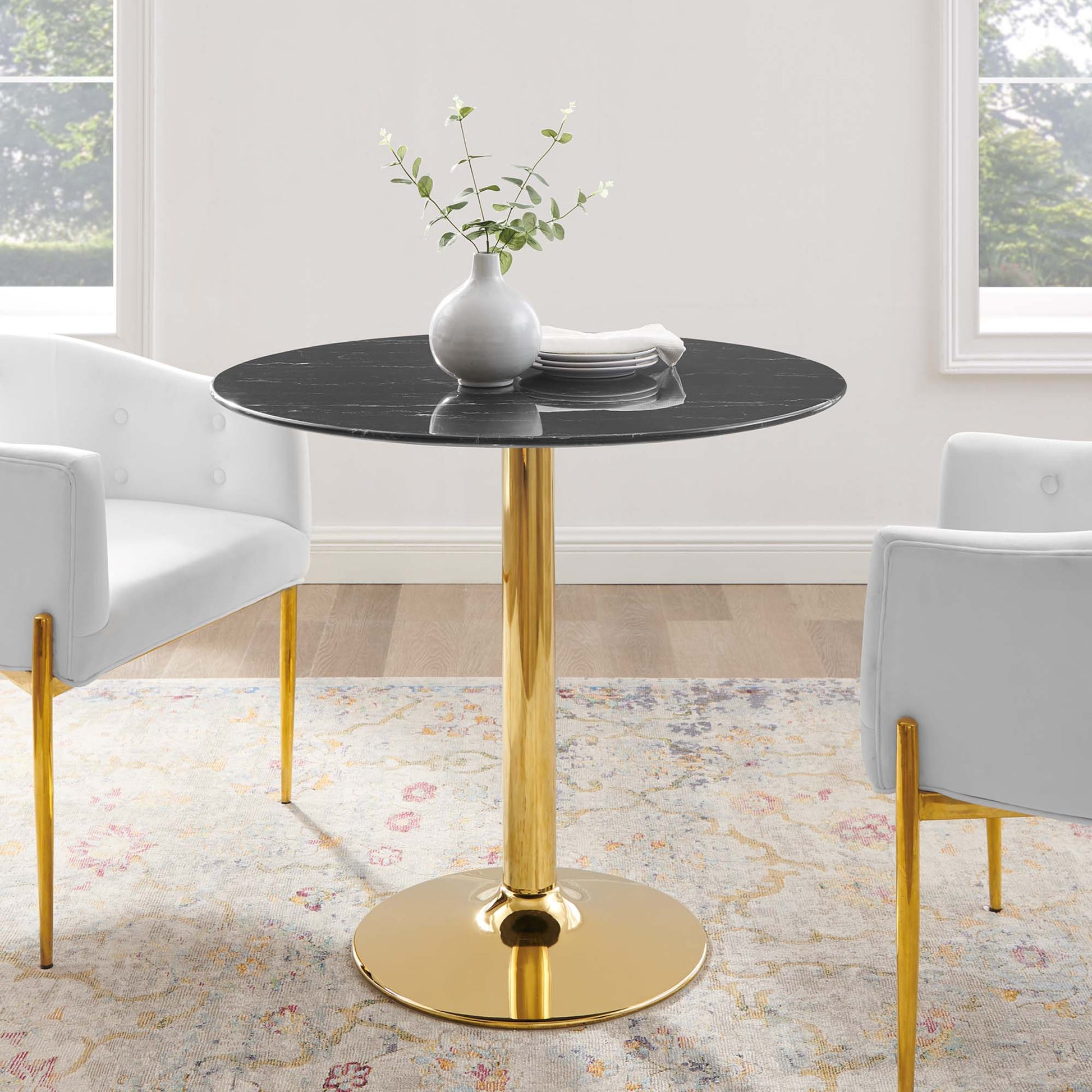 Round black marble-top table on a gold pedestal base with white upholstered chairs and a vase centerpiece.
