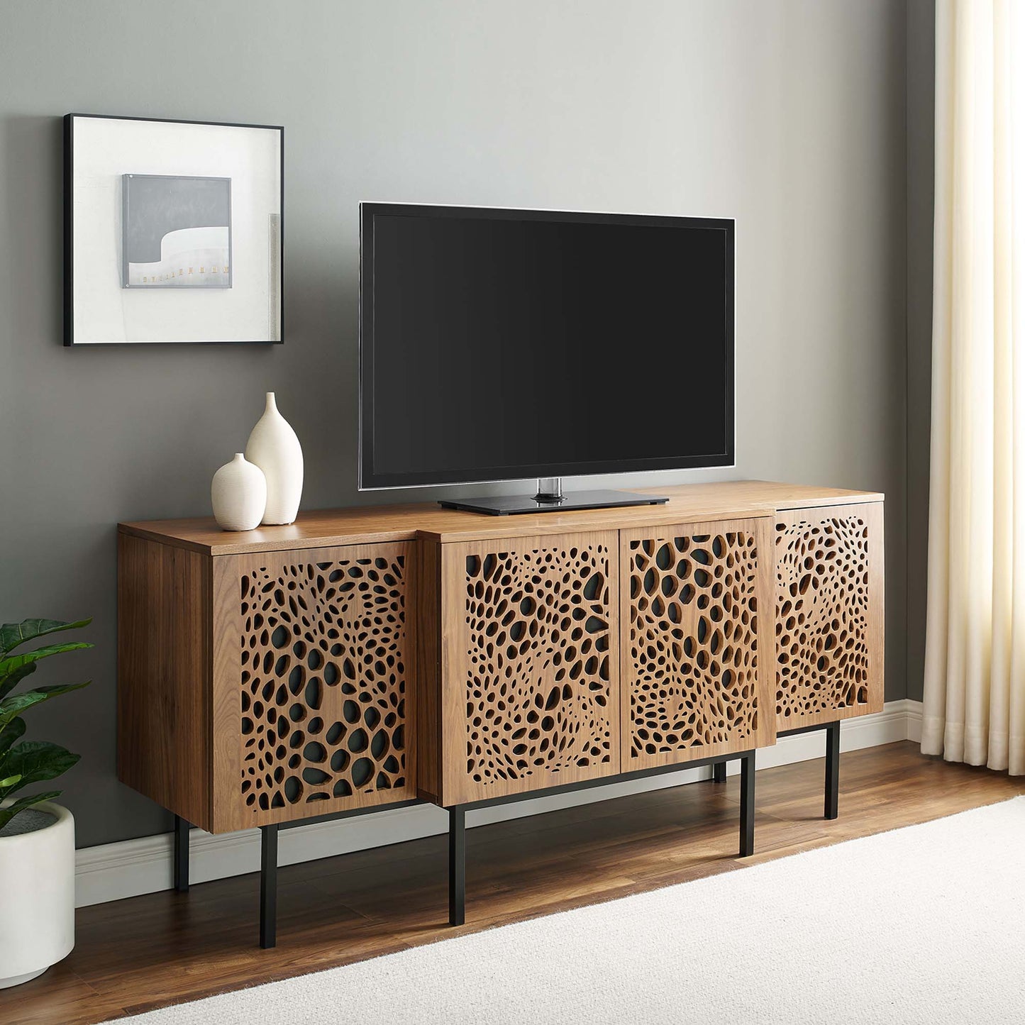 Walnut sideboard with four lattice-cut cabinet doors, circular cutout panels, black metal legs, top surface with two white vases.